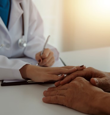 doctor holds the patient's hand supportively while writing the treatment plan for their recovery