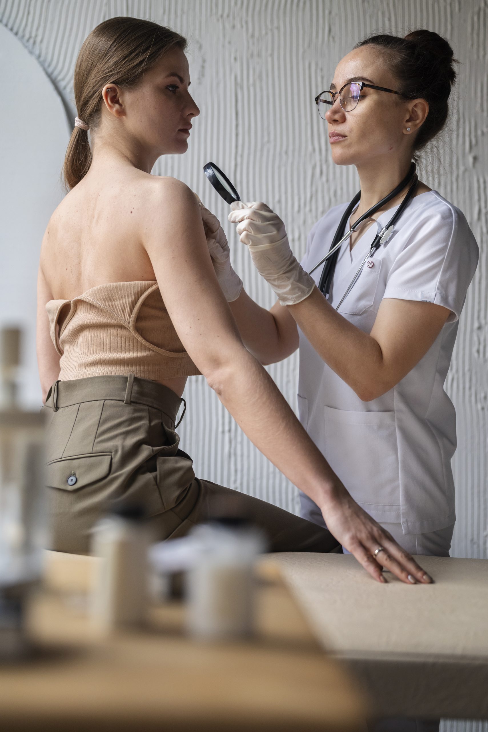 A doctor examines a patient's shoulder, assessing her skin for scar revision procedure in a medical clinic.
