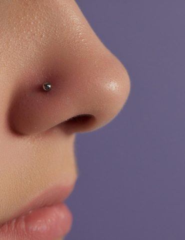Side profile close-up of a nose with a small silver stud piercing against a purple background