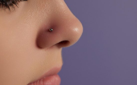 Side profile close-up of a nose with a small silver stud piercing against a purple background