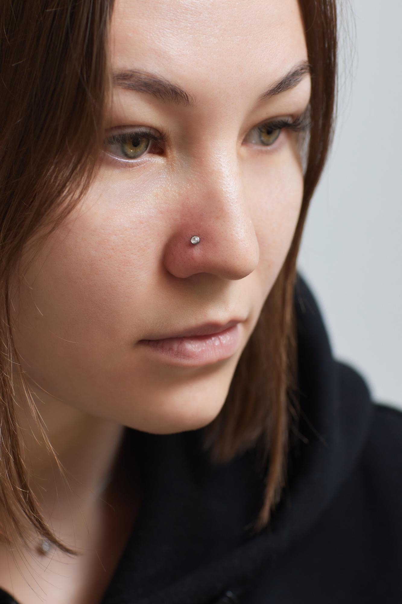 Portrait of a young woman with a small nose stud piercing and red irritation around the nostril
