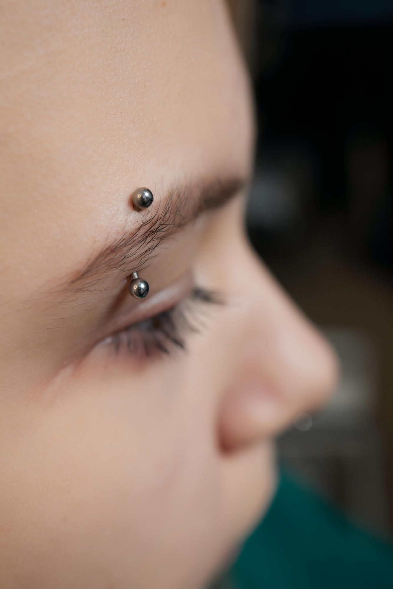 Side profile close-up of an eyebrow piercing with a silver curved barbell.